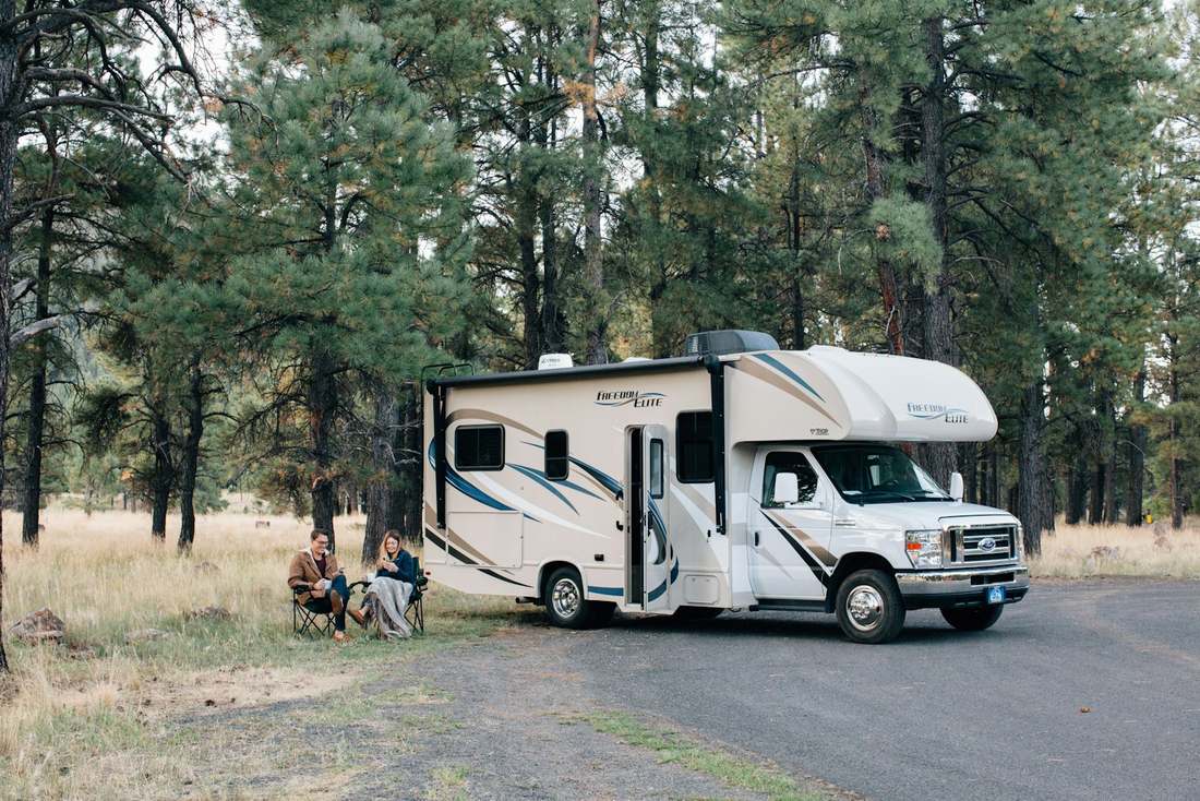 Two RV owners relaxing beside their motorhome at a forest campsite